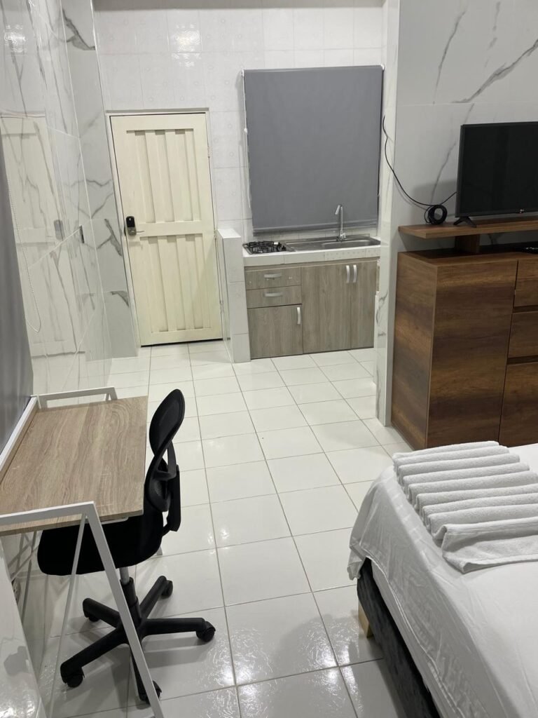 Un apartaestudio amoblado en Cali con un diseño moderno y acogedor. El espacio cuenta con una cama doble con ropa de cama elegante, una sala pequeña con un sofá cómodo, una mesa de comedor para dos personas y una cocina equipada con electrodomésticos y utensilios.