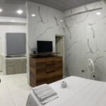 Un apartaestudio amoblado en Cali con un diseño moderno y acogedor. El espacio cuenta con una cama doble con ropa de cama elegante, una sala pequeña con un sofá cómodo, una mesa de comedor para dos personas y una cocina equipada con electrodomésticos y utensilios.