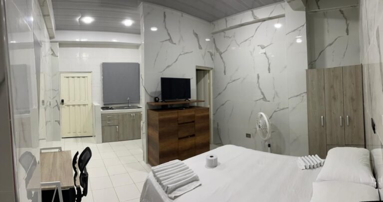 Un apartaestudio amoblado en Cali con un diseño moderno y acogedor. El espacio cuenta con una cama doble con ropa de cama elegante, una sala pequeña con un sofá cómodo, una mesa de comedor para dos personas y una cocina equipada con electrodomésticos y utensilios.