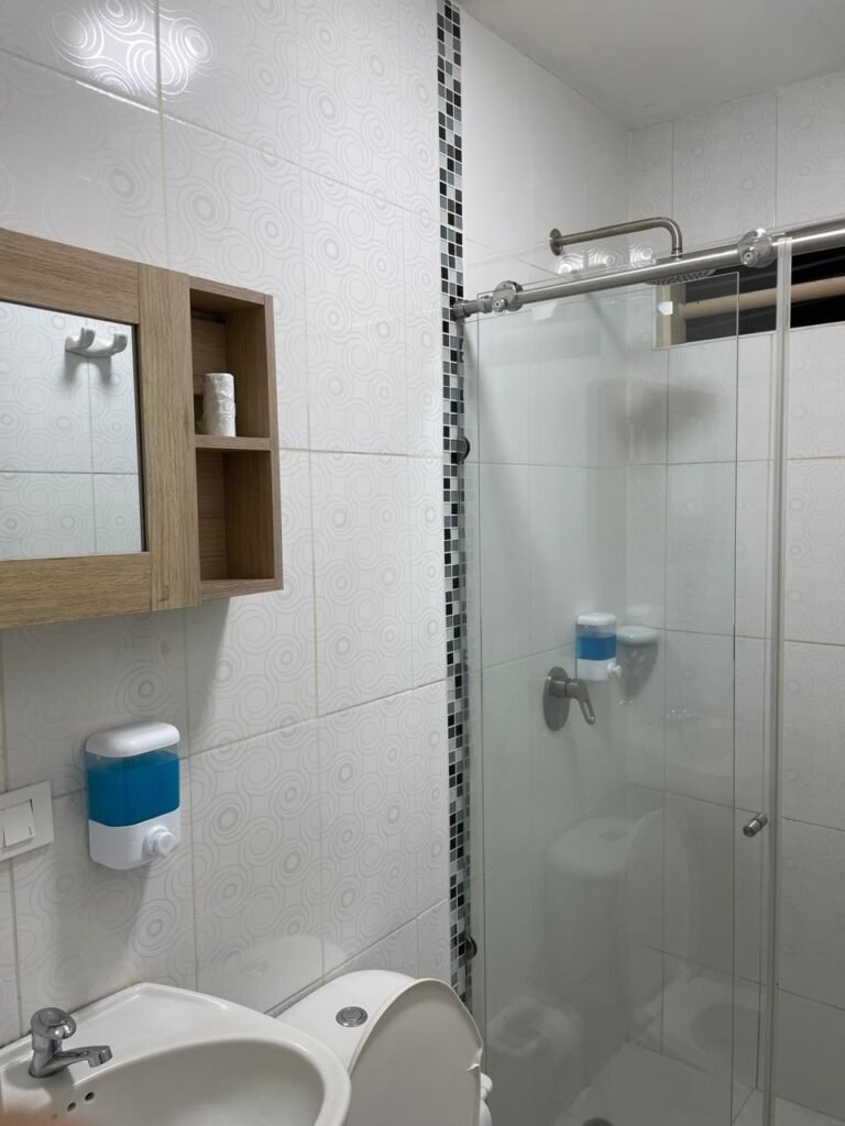 Un apartaestudio amoblado en Cali con un diseño moderno y acogedor. El espacio cuenta con una cama doble con ropa de cama elegante, una sala pequeña con un sofá cómodo, una mesa de comedor para dos personas y una cocina equipada con electrodomésticos y utensilios.