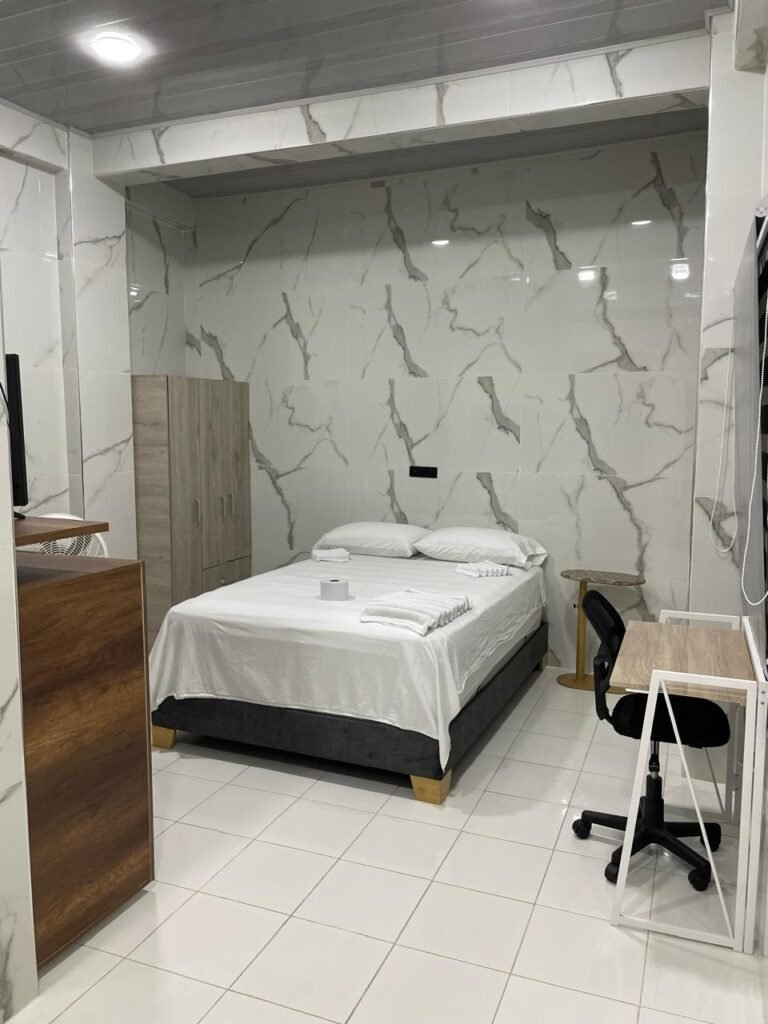 Un apartaestudio amoblado en Cali con un diseño moderno y acogedor. El espacio cuenta con una cama doble con ropa de cama elegante, una sala pequeña con un sofá cómodo, una mesa de comedor para dos personas y una cocina equipada con electrodomésticos y utensilios.